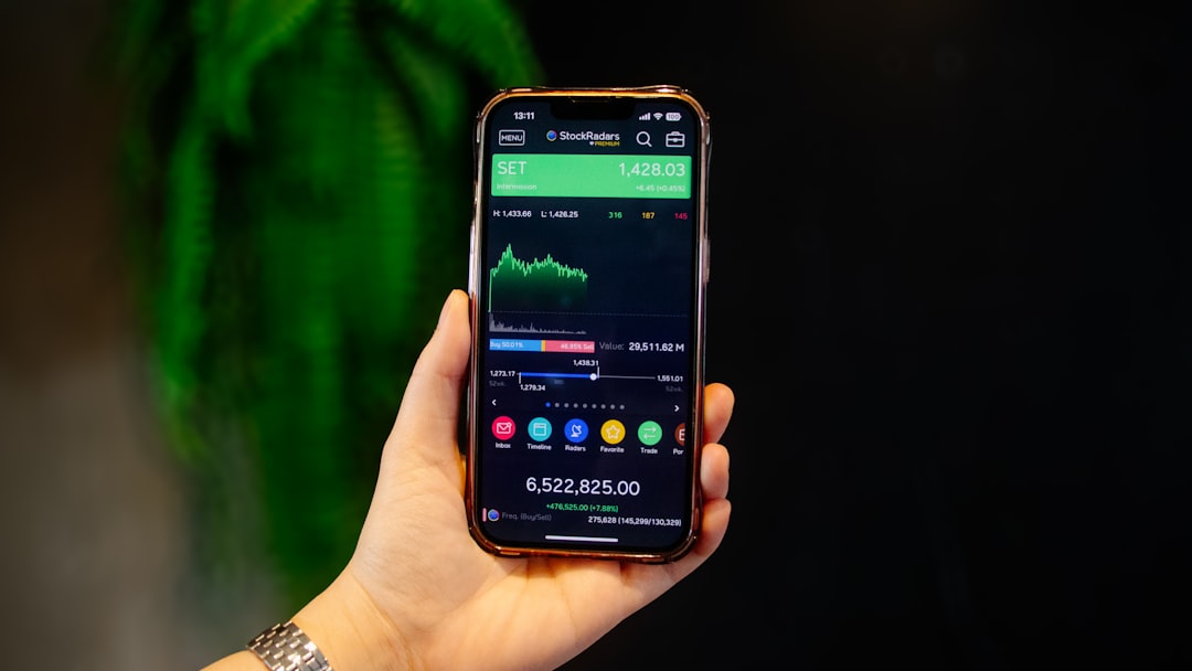 Main tenant un smartphone avec un tableau de bord d’analyse des marchés boursiers et du portefeuille affiché à l’écran